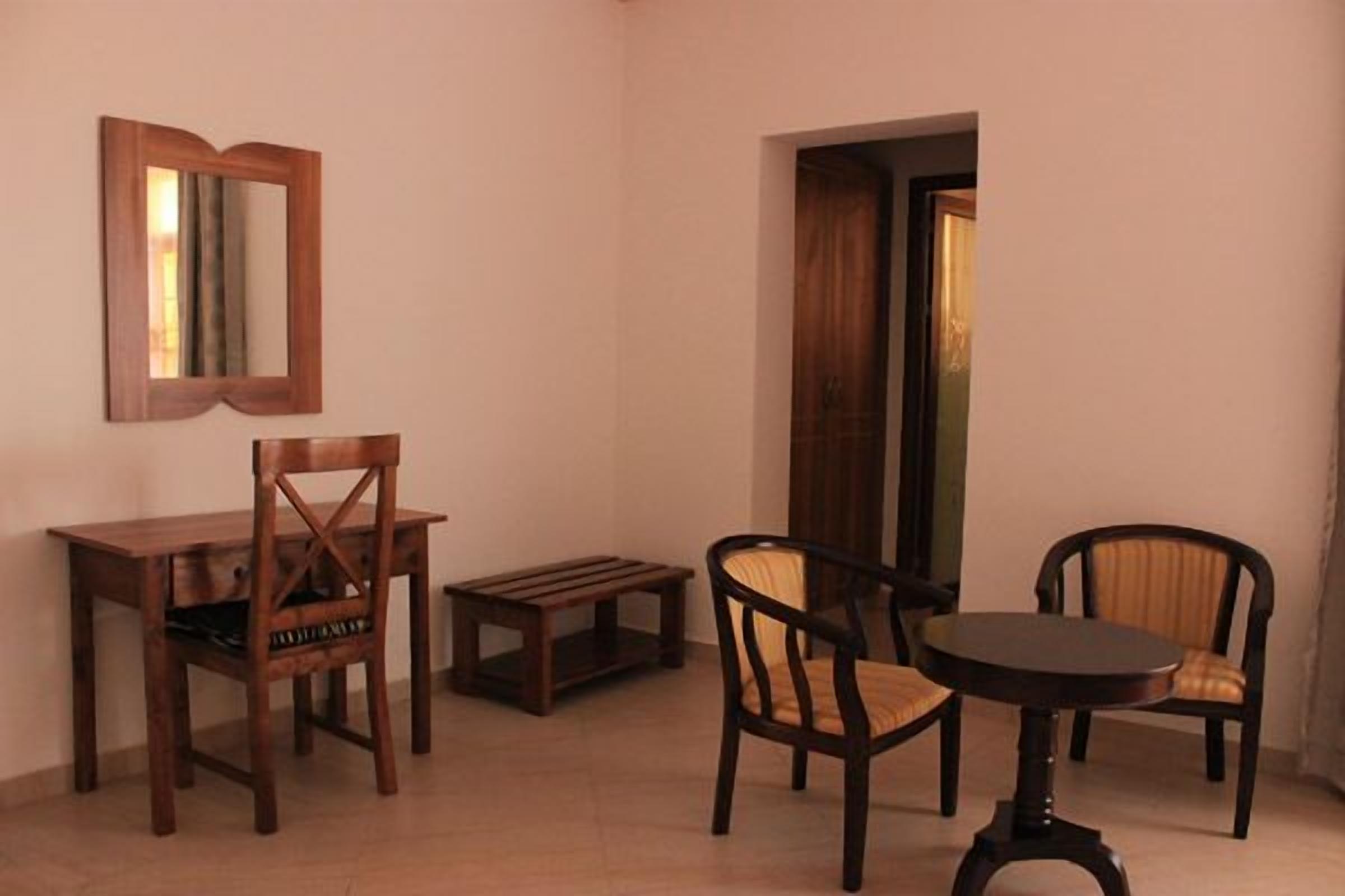 A room with a wooden dining table, two chairs, a small bench, and a mirror on the wall.