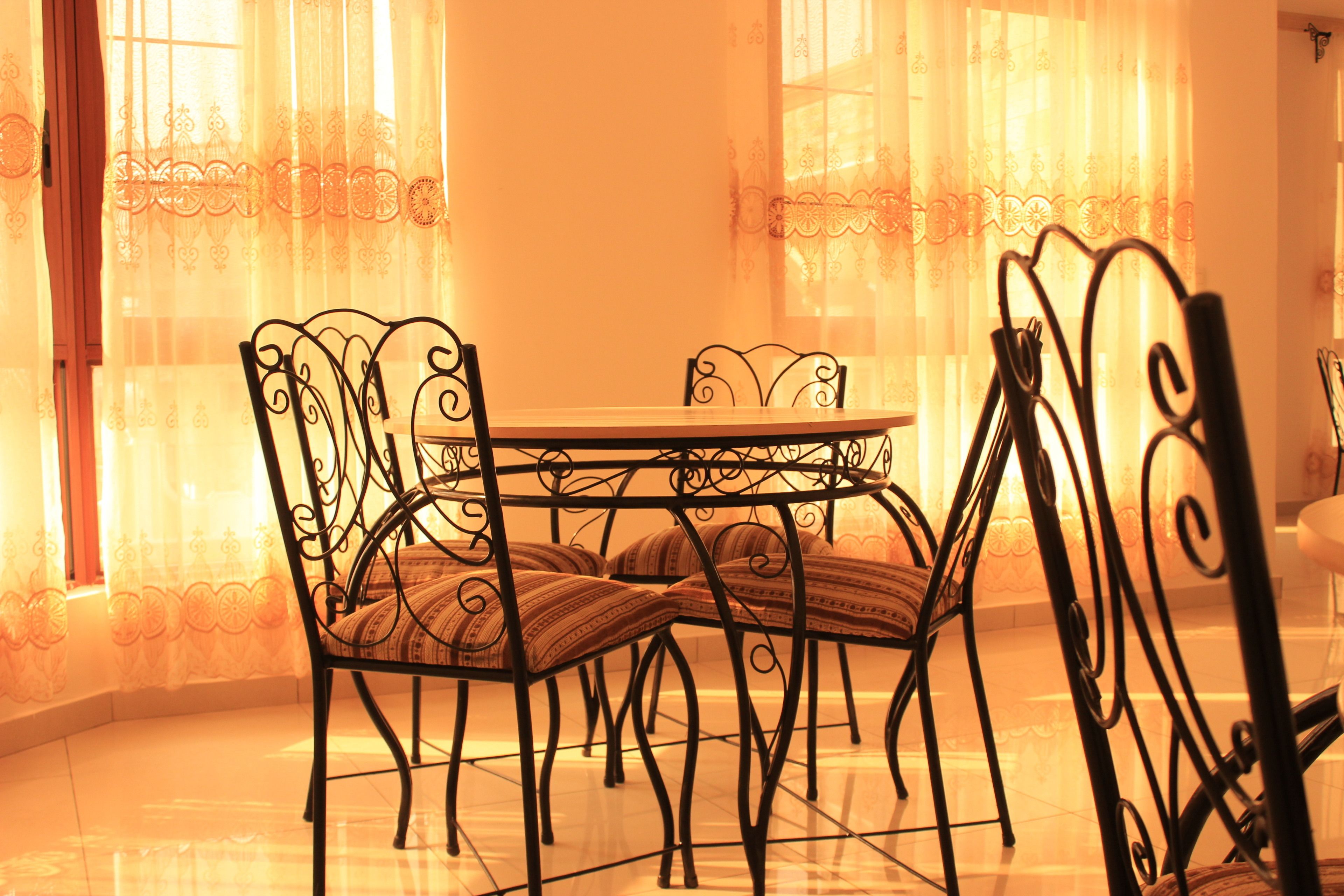 A dining area with a round table and four chairs with intricate metal frames.