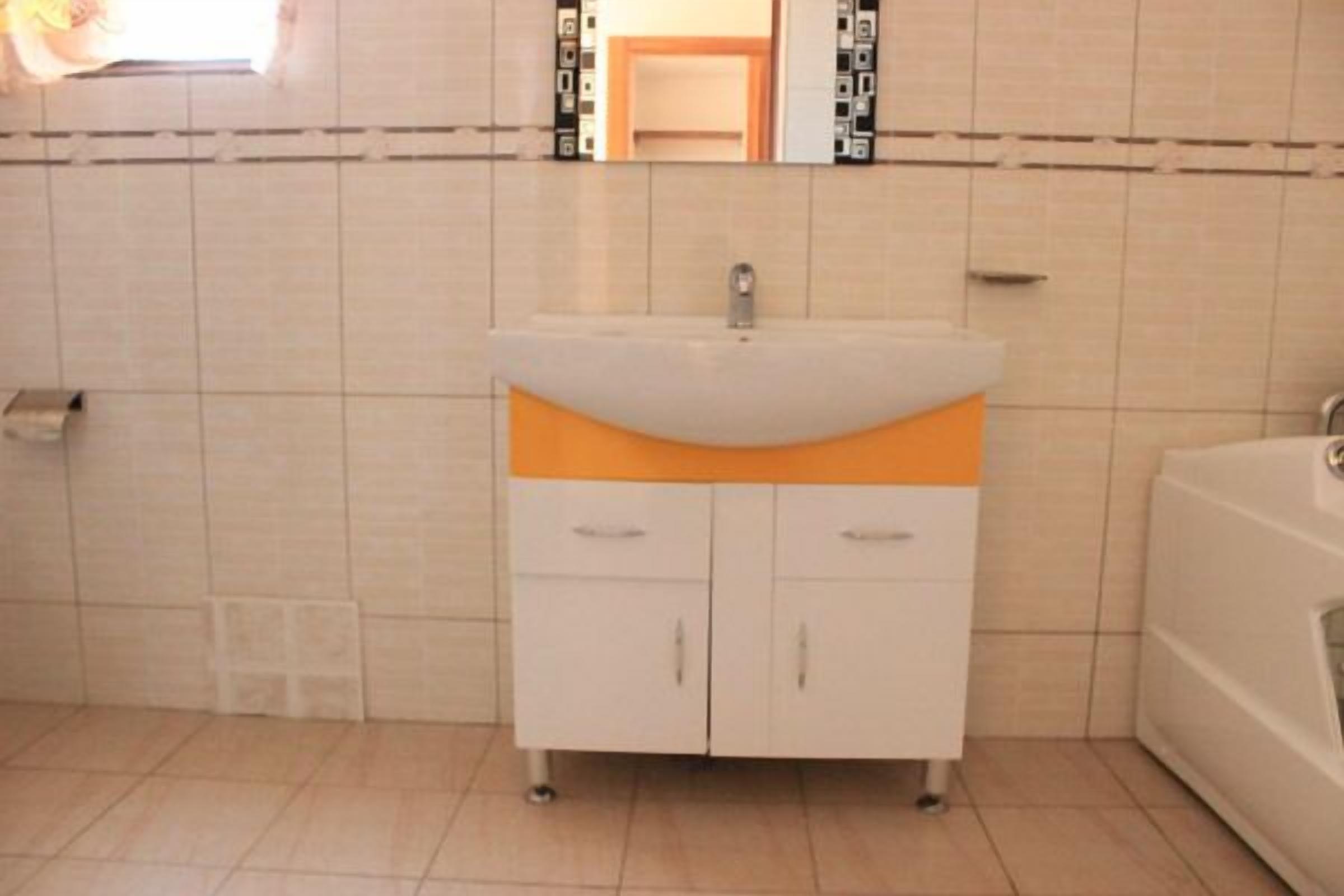Ein Badezimmer mit einem weißen Waschbecken, einer orangefarbenen Arbeitsplatte und einem Spiegel darüber.