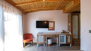 Et værelse med trælofter, et fladskærms-tv ophængt på væggen, et træskab med et lille køleskab, en rød stol og en seng.