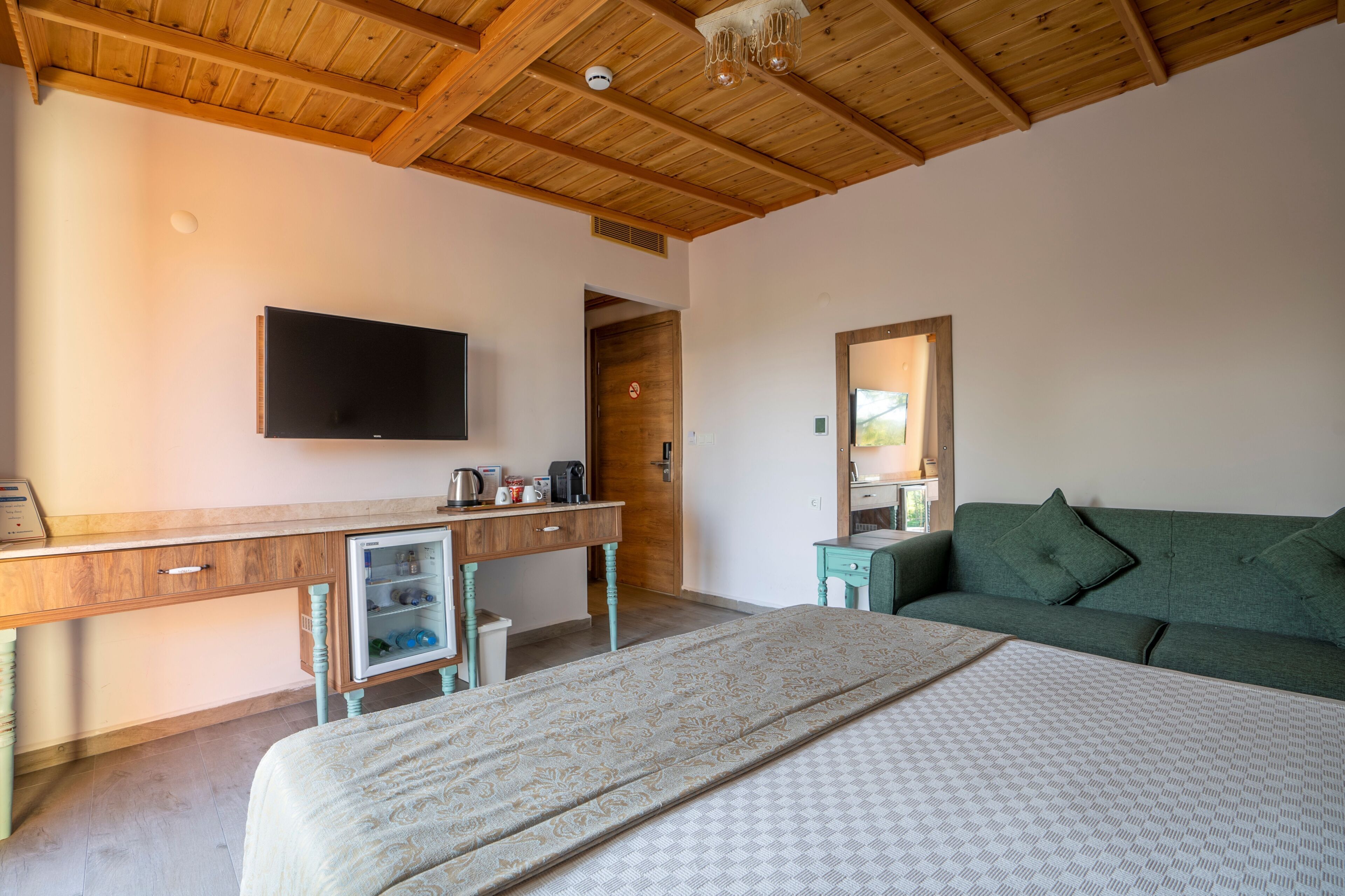 Un dormitorio con cama, un escritorio con televisor, un sofá verde y techo de madera.