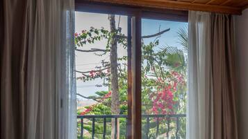 A room with a bed, wooden ceiling, and a view of a balcony with plants and flowers.