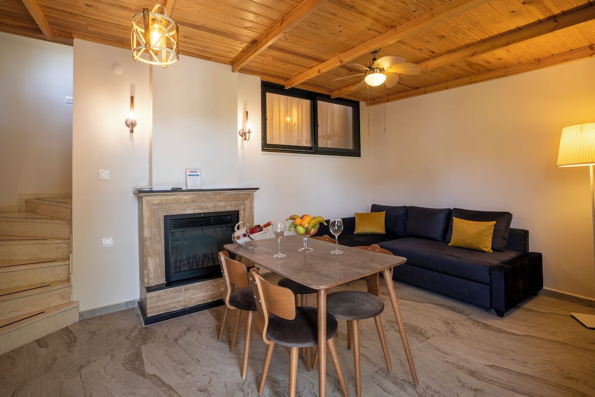 Ein Essbereich mit Holztisch und Stühlen, einem Kamin und einer Couch mit Kissen.