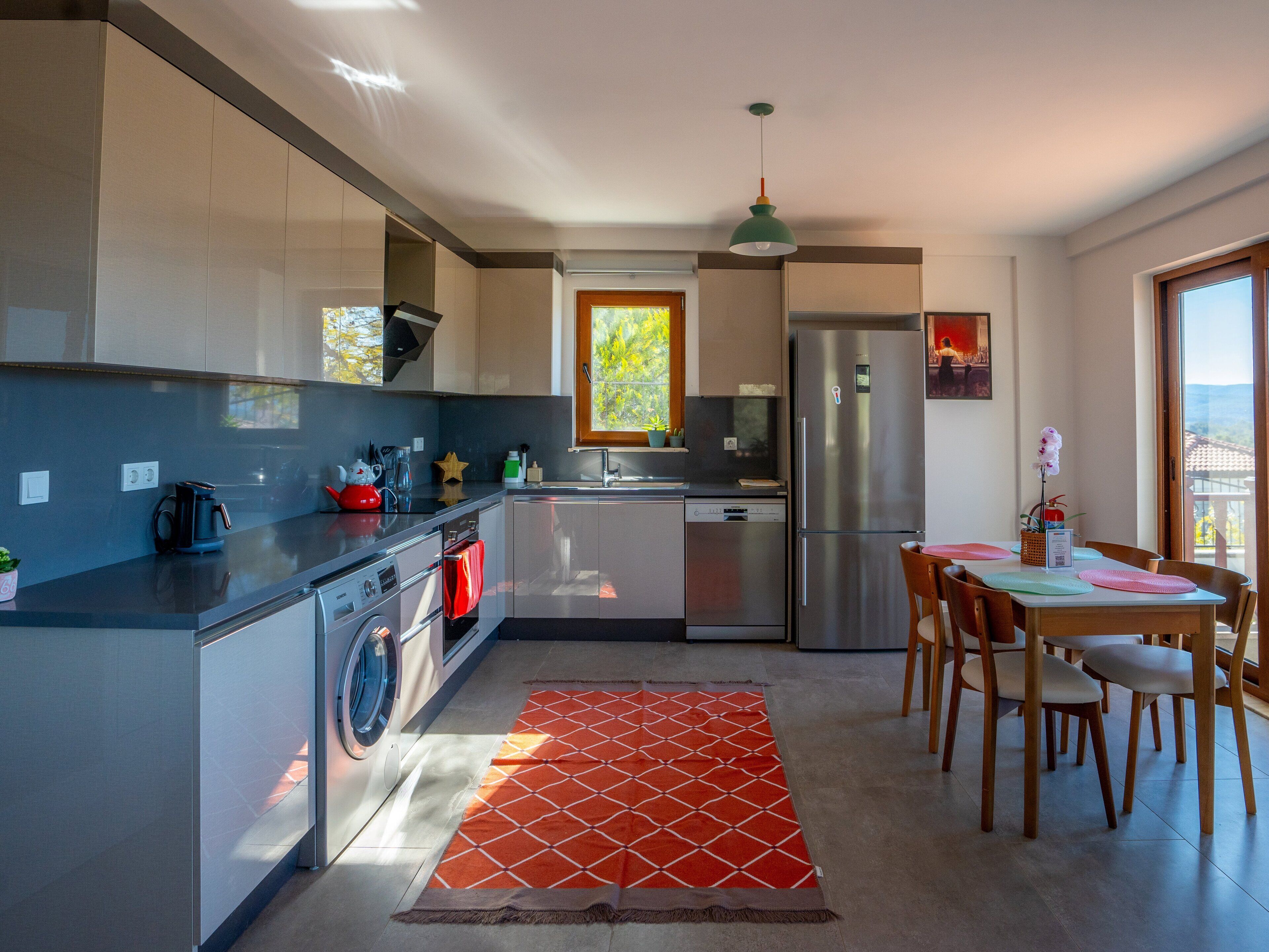 A modern kitchen with a washing machine, a refrigerator, and a dining area with chairs and a table.