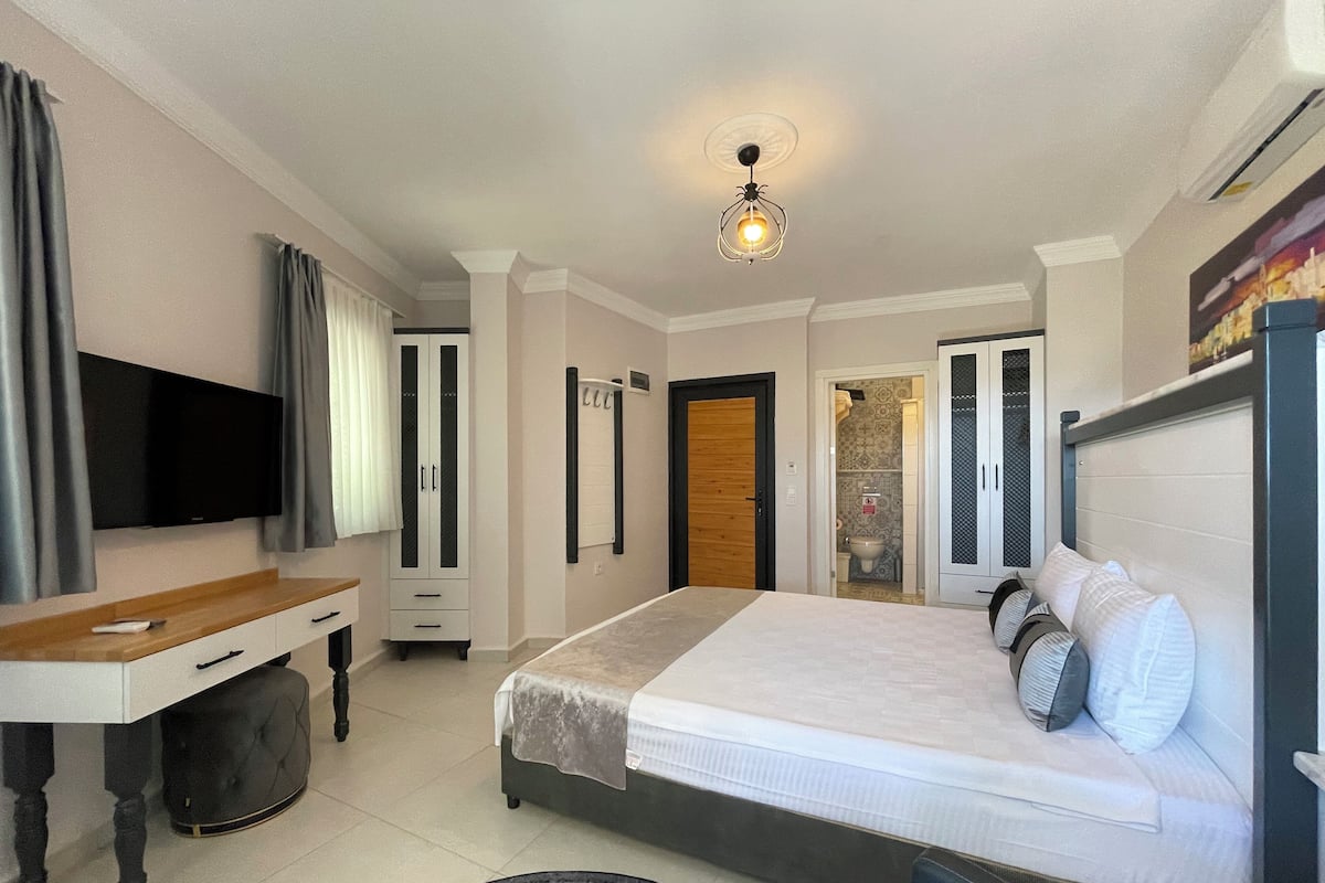 Ein Hotelzimmer mit Bett, Fernseher, Schreibtisch und einem durch eine offene Tür einsehbaren Badezimmer.