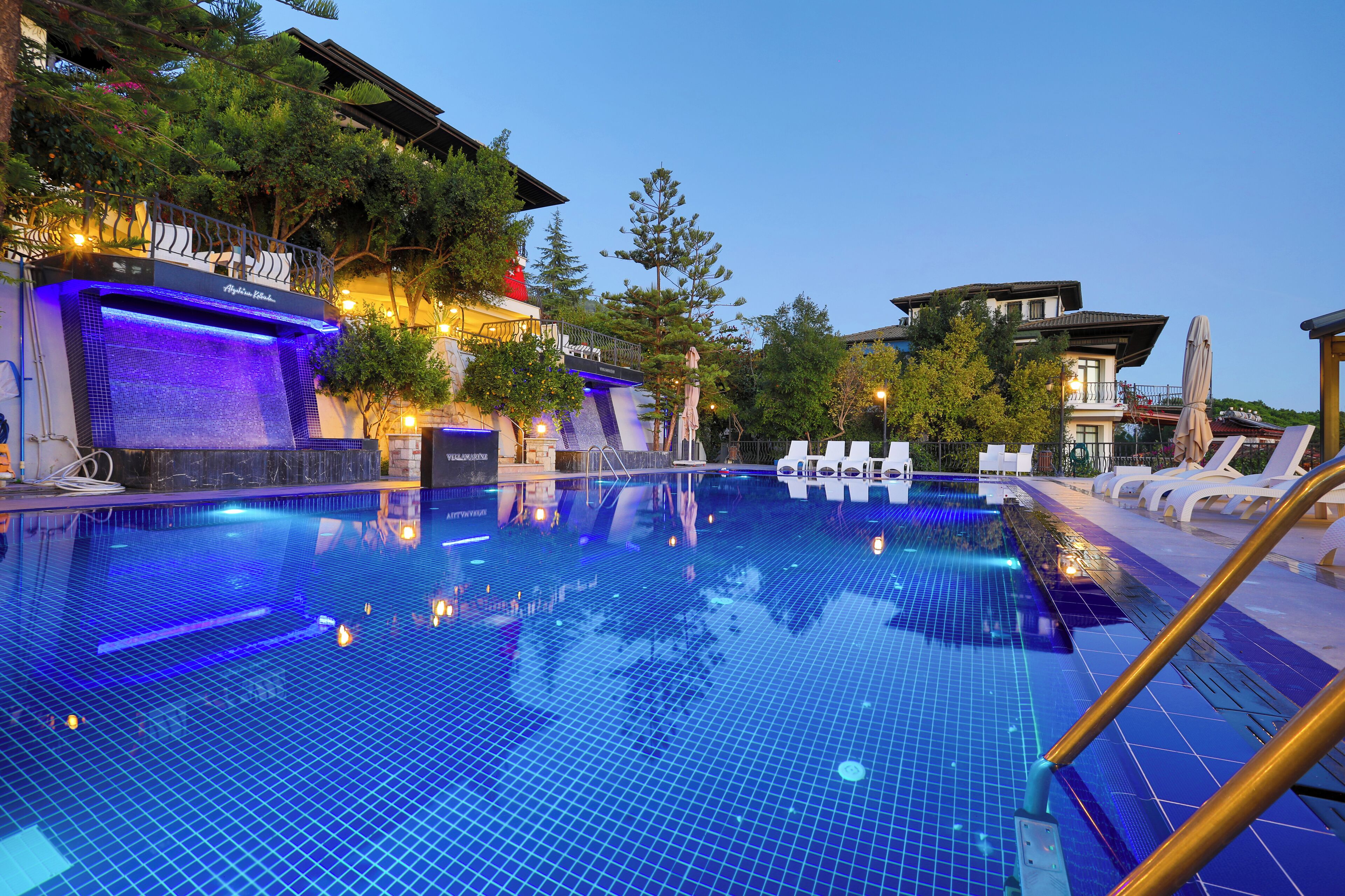 A swimming pool with blue tiles, lounge chairs, and a waterfall feature.