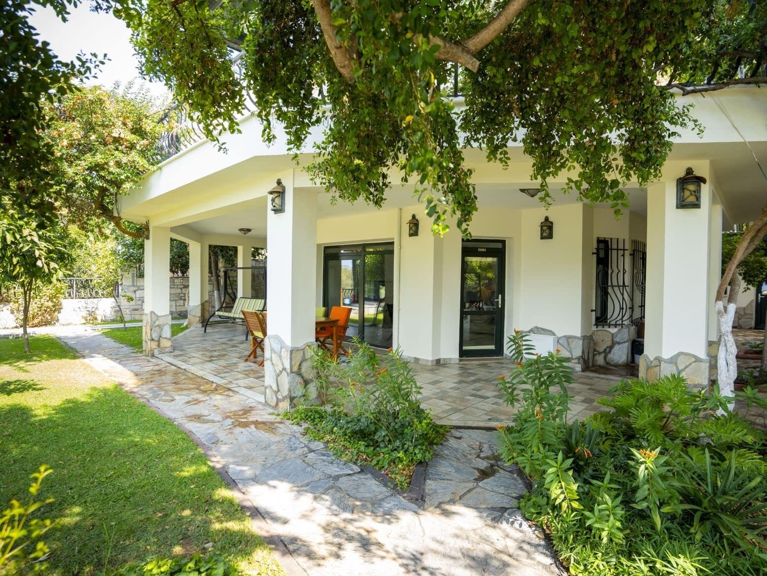 A covered outdoor area with stone flooring, a seating arrangement, and a door leading to the interior.