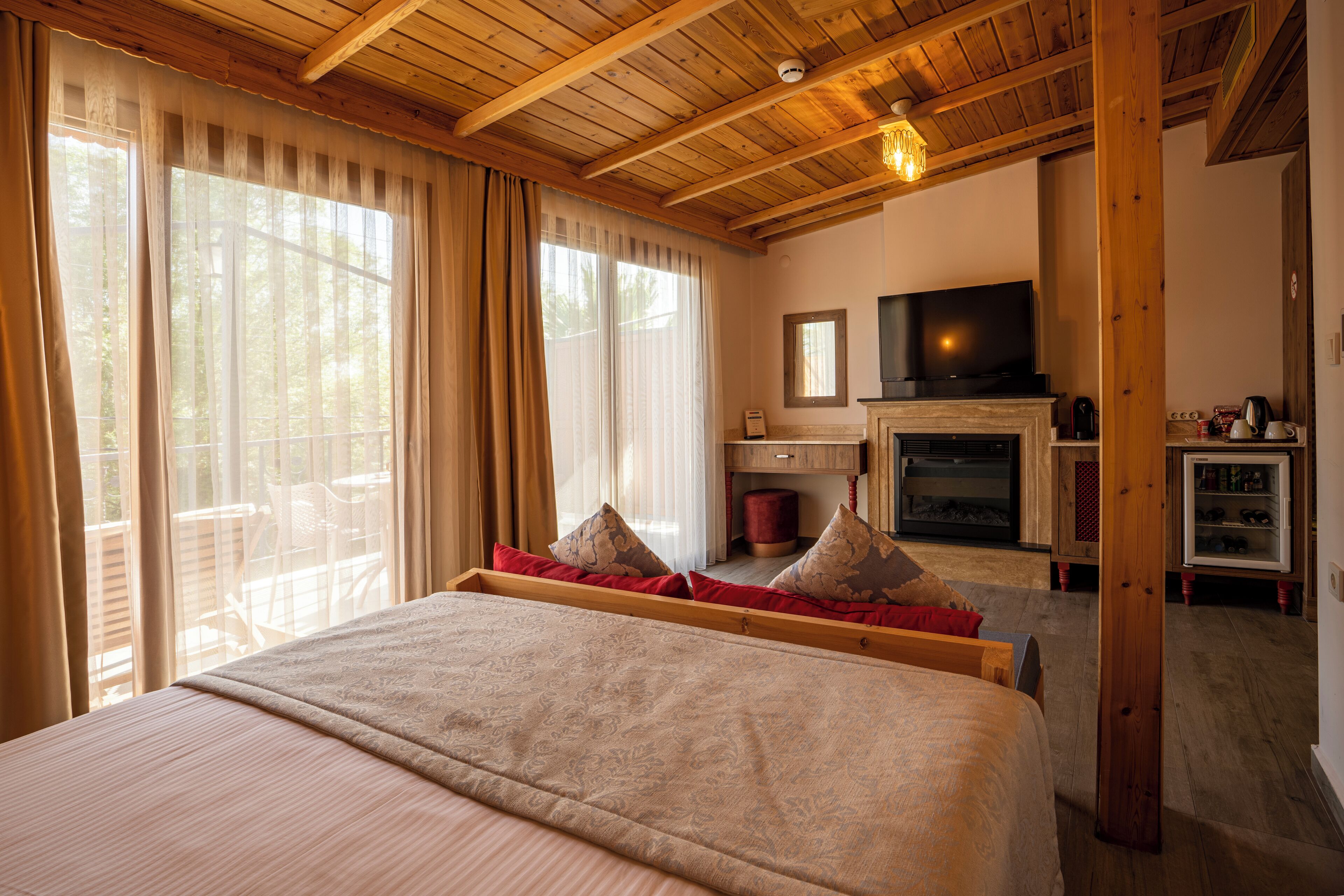A bedroom with a large bed, a television, a fireplace, and a balcony with outdoor furniture.