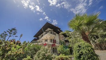 Ein mehrgeschossiges Gebäude mit Balkonen, umgeben von üppigem Grün und blauem Himmel.
