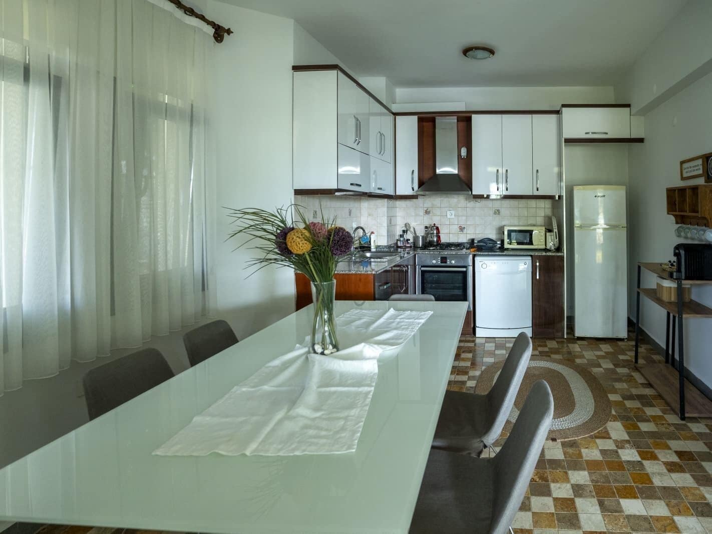A modern kitchen with white cabinets, a dining table with a vase of flowers, and a checkered floor.
