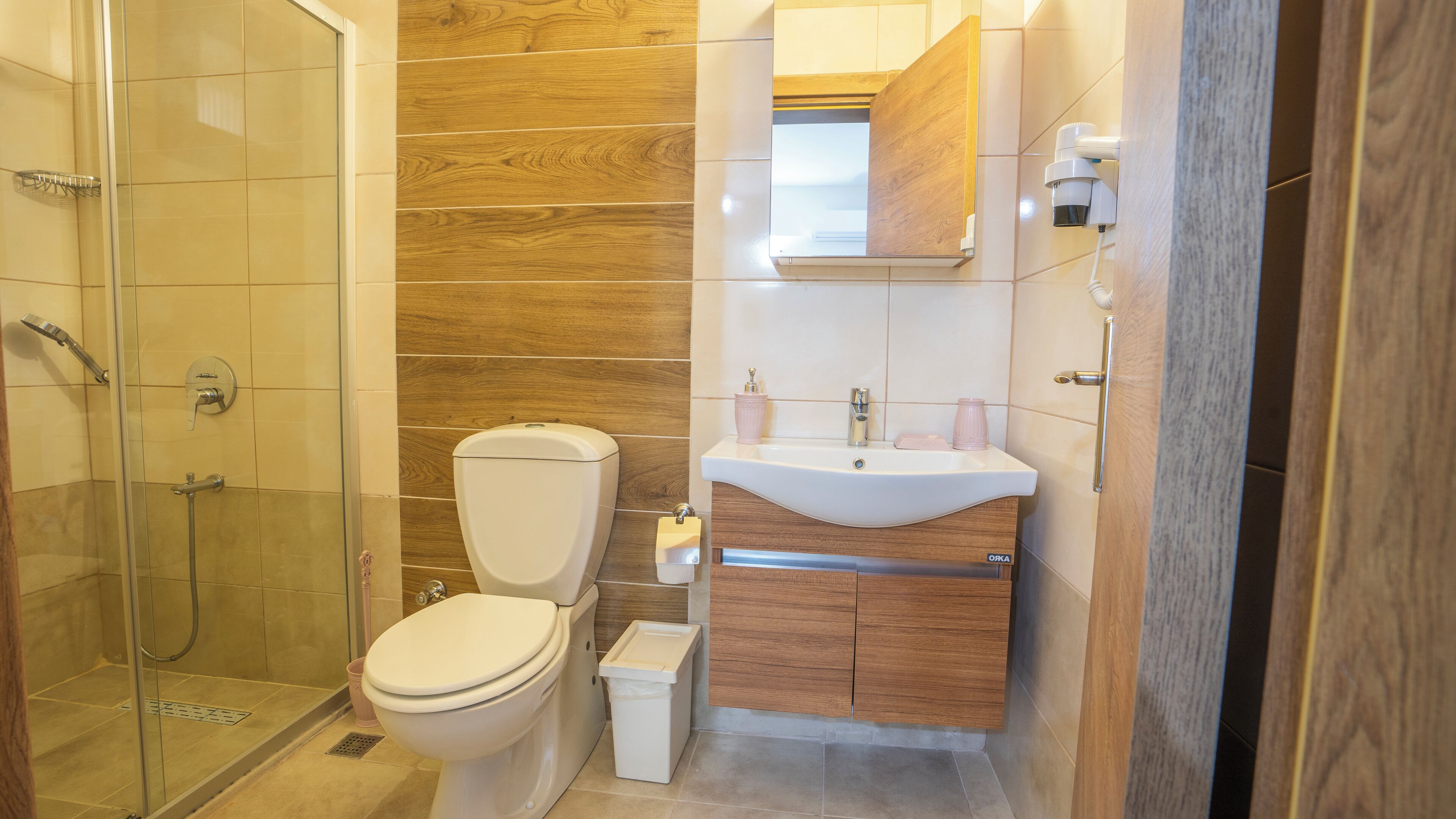 Un baño moderno con cabina de ducha de vidrio, inodoro, lavabo con gabinete de madera y espejo sobre el lavabo.