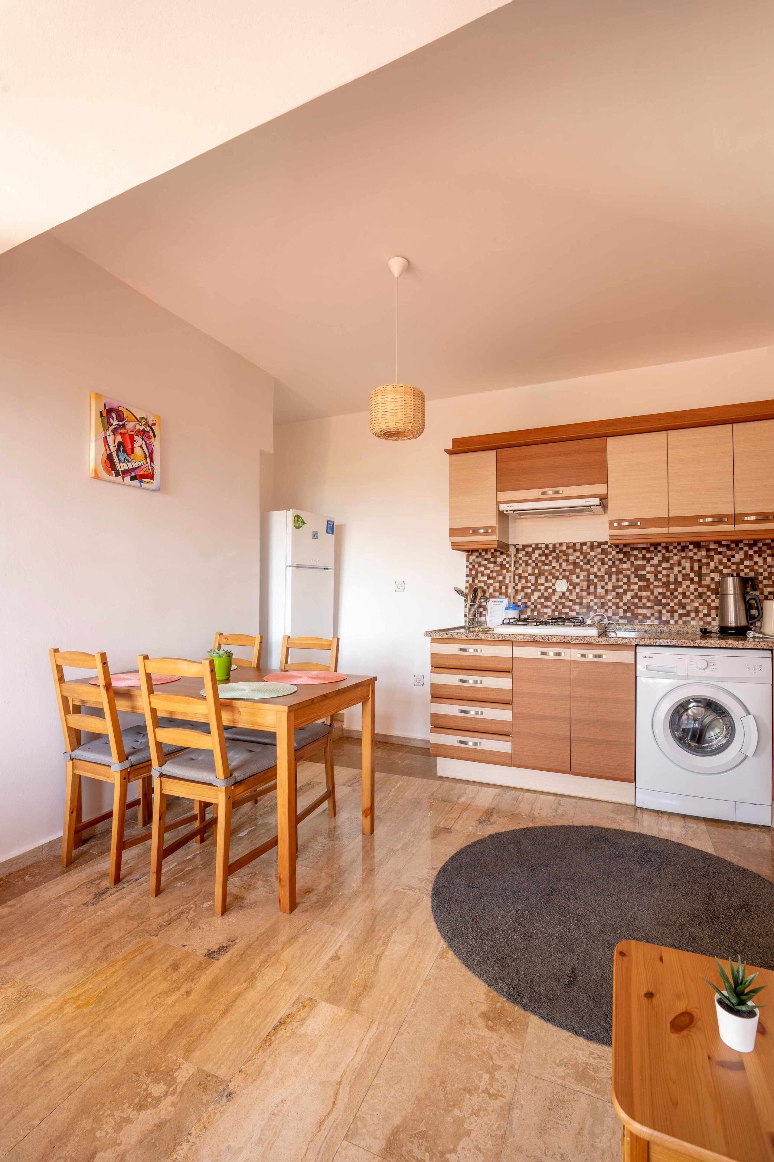 Una cocina compacta con armarios de madera, lavadora integrada y un comedor con mesa y sillas.
