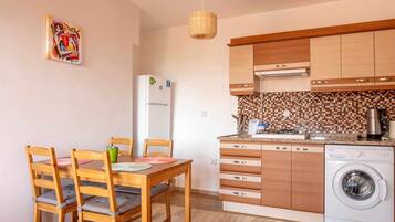 Una cocina compacta con armarios de madera, lavadora integrada y un comedor con mesa y sillas.