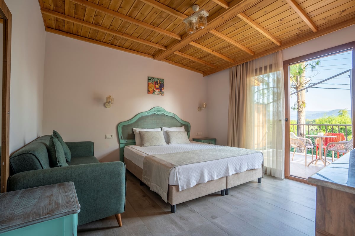 Ein Schlafzimmer mit Bett, einer Couch, einem Nachttisch und Blick ins Freie.