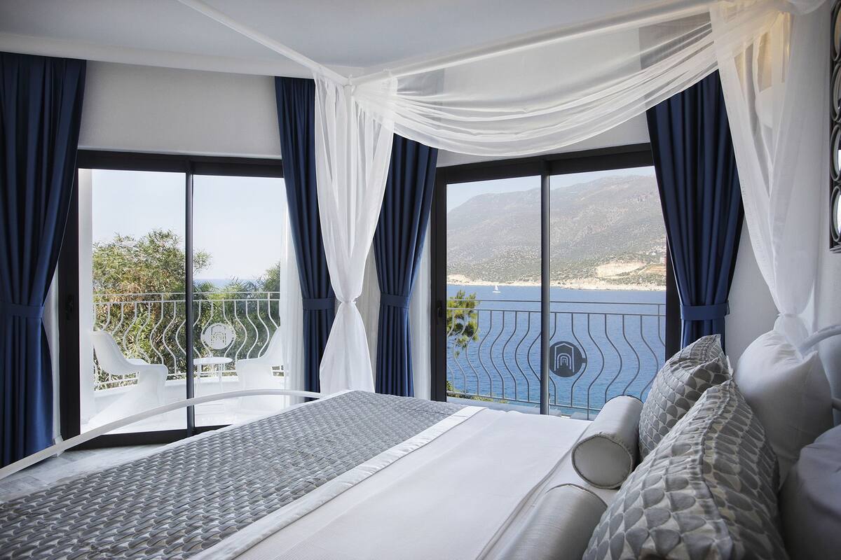 A bedroom with a large bed, a view of the sea, and a balcony with a railing.