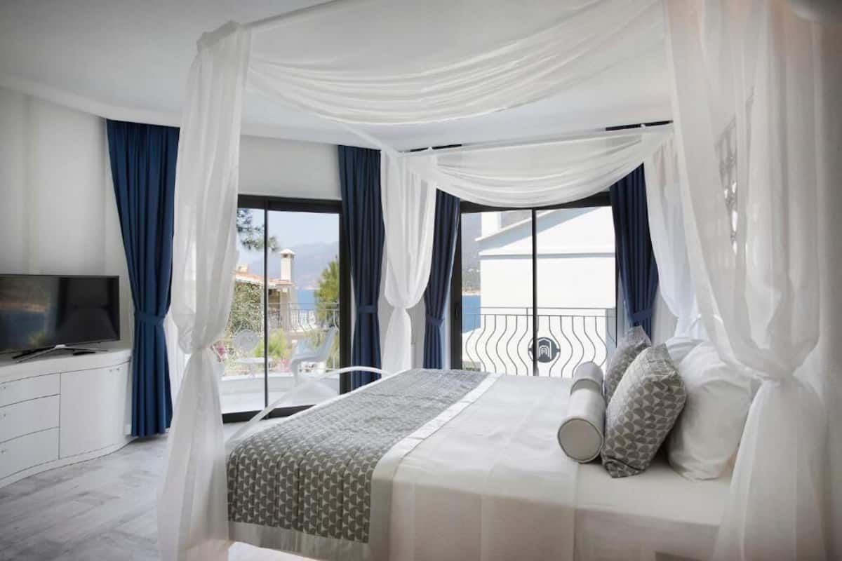 A bedroom with a bed, curtains, a TV, and a balcony with a view.