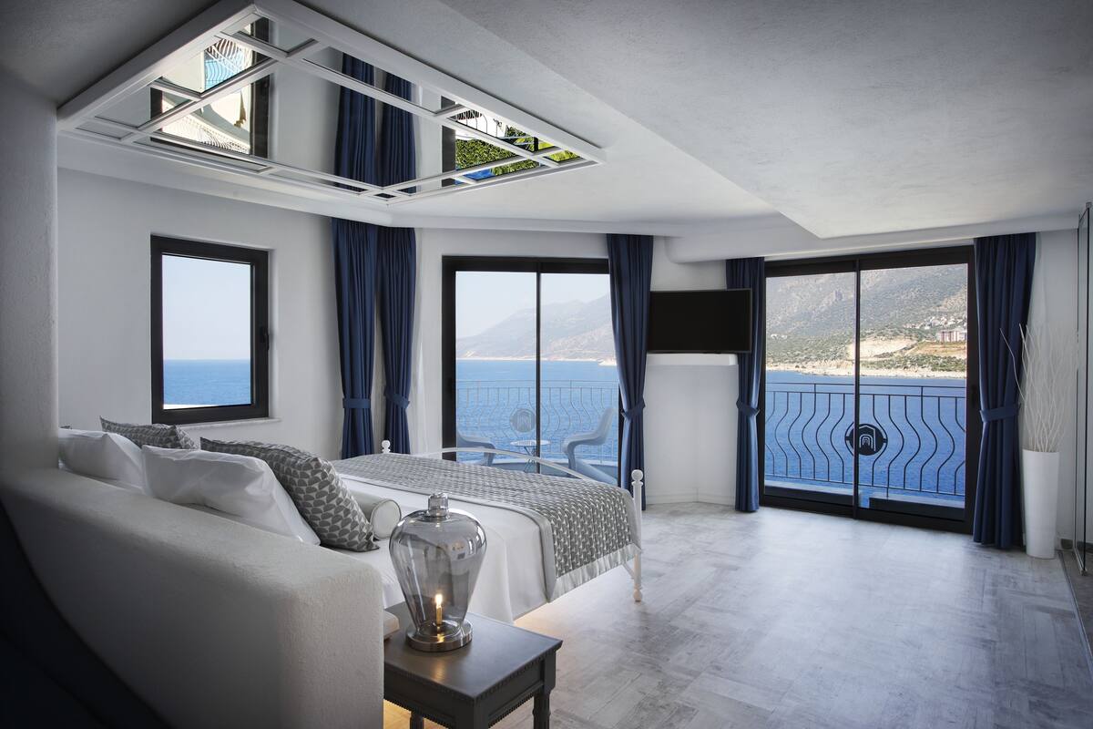A modern bedroom with a large bed, a sofa, and a balcony with a view of the sea.