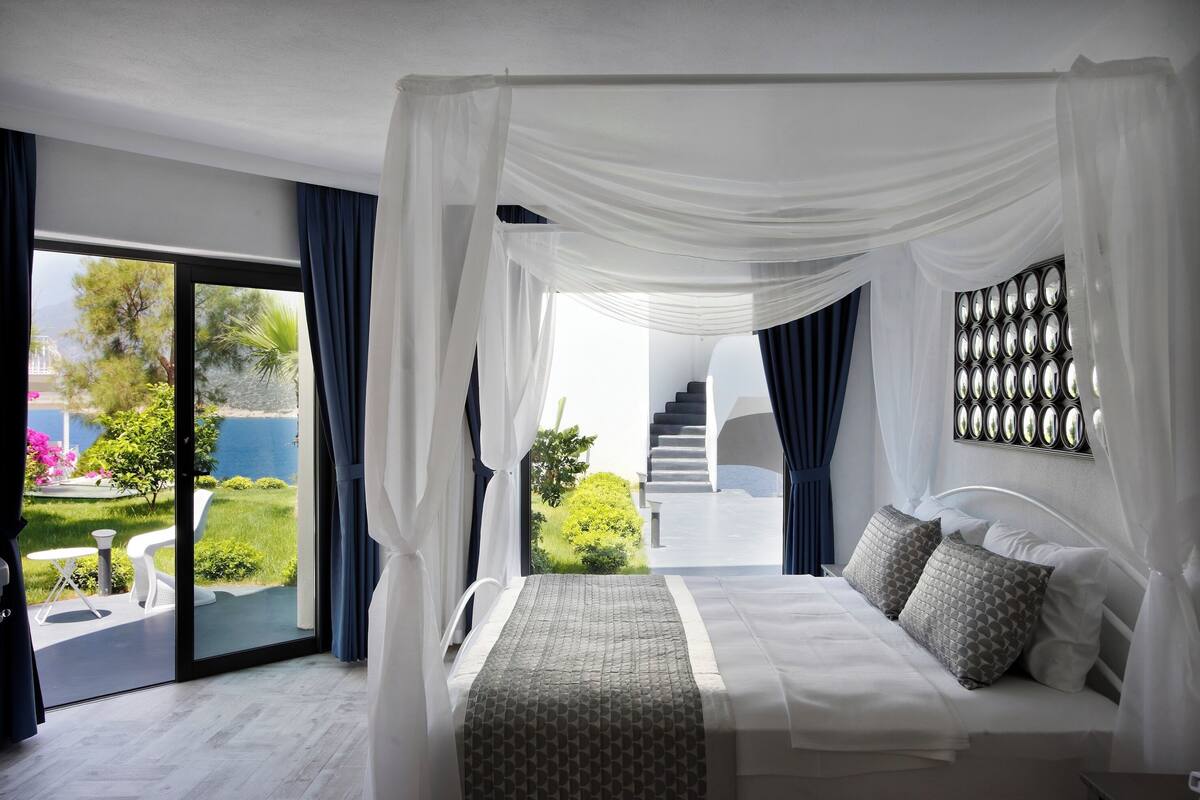 A bedroom with a canopy bed, a view of the outdoors, and a staircase leading to an upper level.