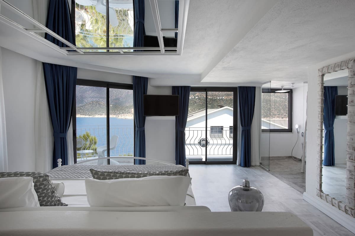 A modern hotel room with a balcony, large windows, and a view of the sea.