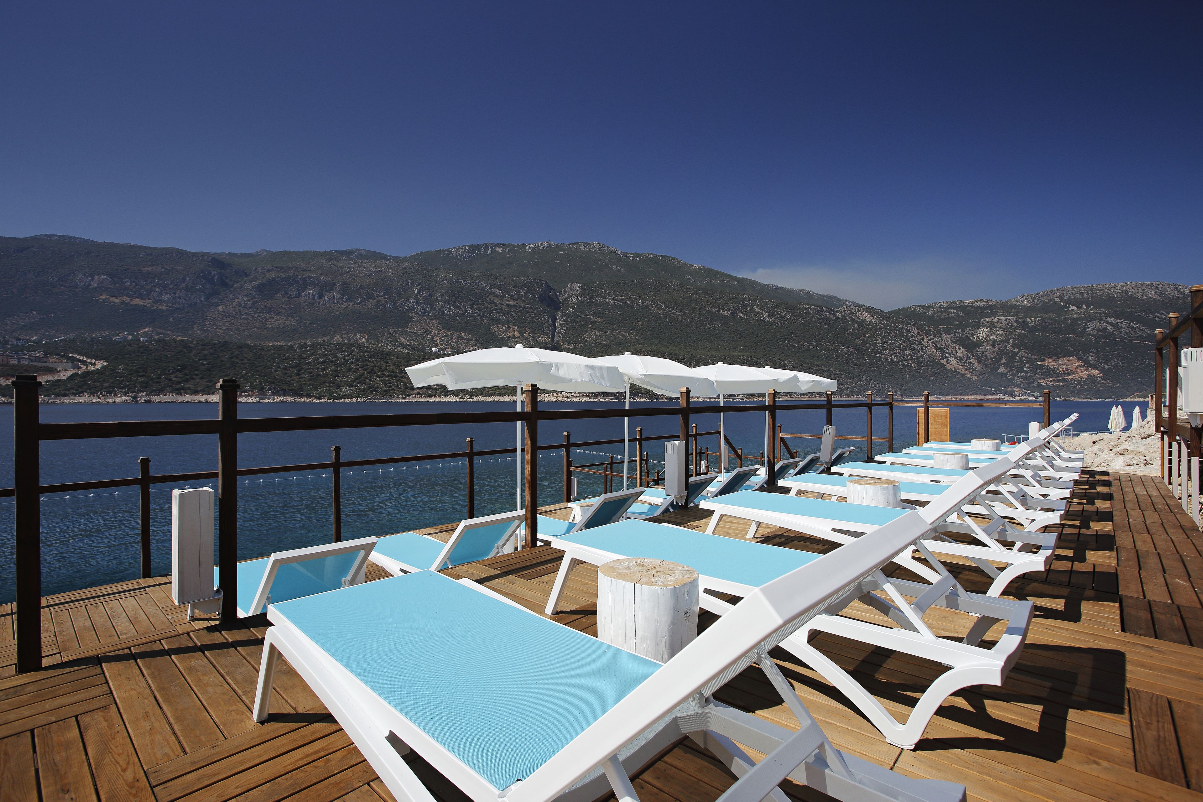 Una terrazza con lettini e ombrelloni con vista su un corpo d'acqua e montagne.
