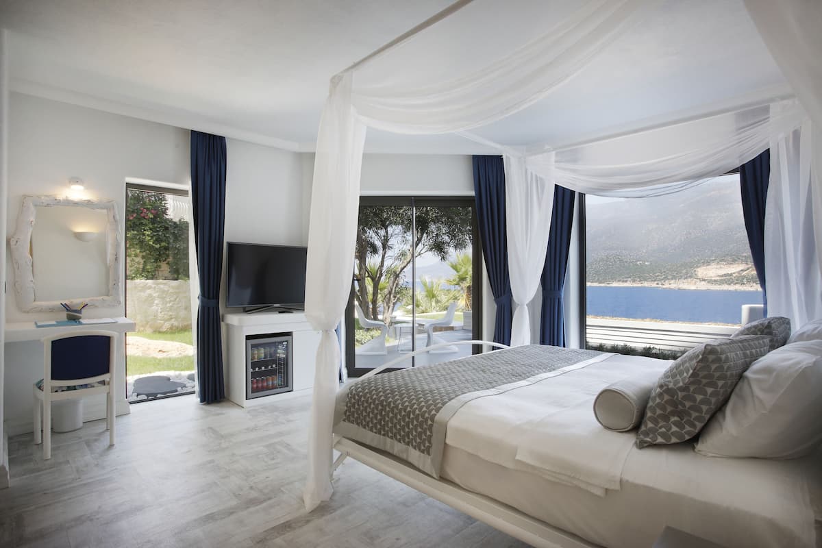 A bedroom with a bed, a TV, a desk, and a view of the sea.