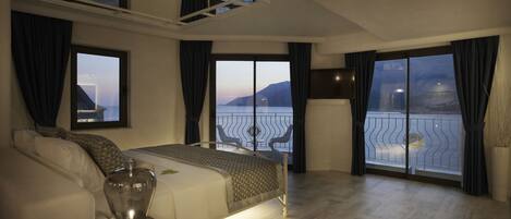 Un dormitorio con una cama grande, una mesita de noche y vistas al mar desde un balcón.