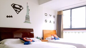 Ein Hotelzimmer mit zwei Betten, einem großen Fenster und Wandbildern mit Superhelden-Motiven.