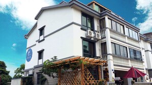 Ein zweistöckiges Gebäude mit weißer Fassade, großen Fenstern und einer Holzpergola mit Pflanzen.