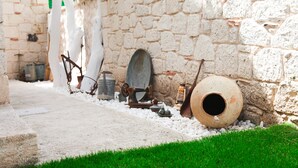 A narrow stone pathway leading to a rustic outdoor area with a stone wall, a large clay pot, and various old metal objects. - Alaçatı 716 Hotel (Cesme)