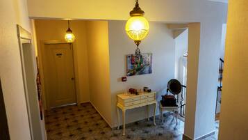 A hallway with patterned flooring, a white door, a small table with decorative items, and a hanging lamp.