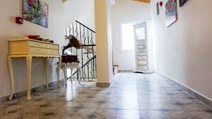 A hallway with a tiled floor, a staircase, a white table with drawers, and a painting on the wall. - Alaçatı 716 Hotel (Cesme)