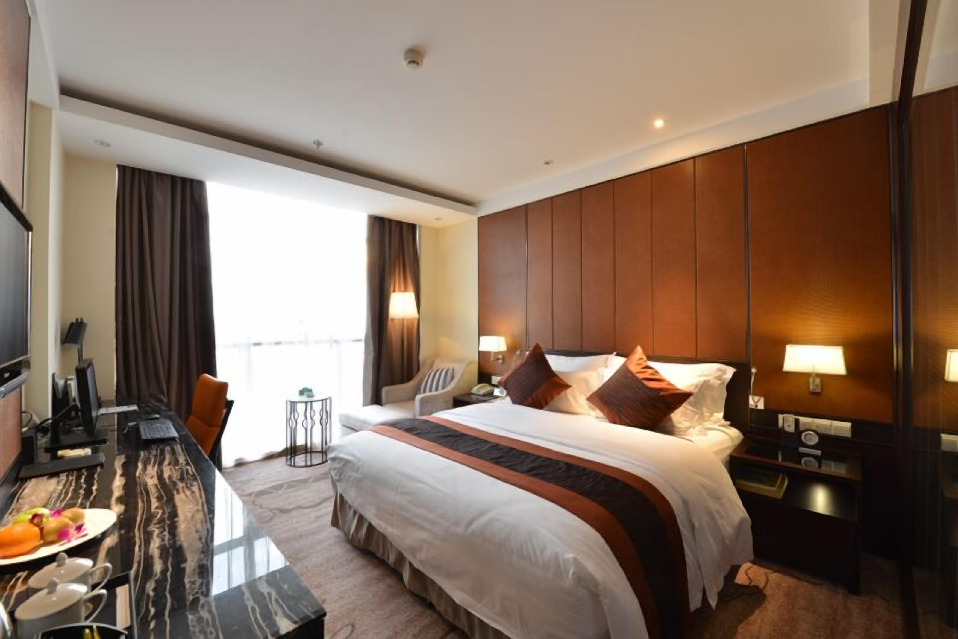 Een hotelkamer met een groot bed, een bureau met een computer, een stoel en een kleine tafel met een lamp.