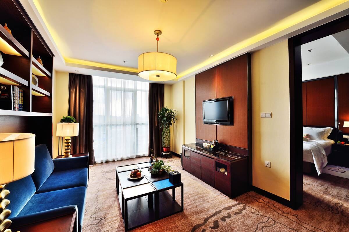 Una habitación de hotel con sofá, mesa de centro, televisor, cama y estantería.