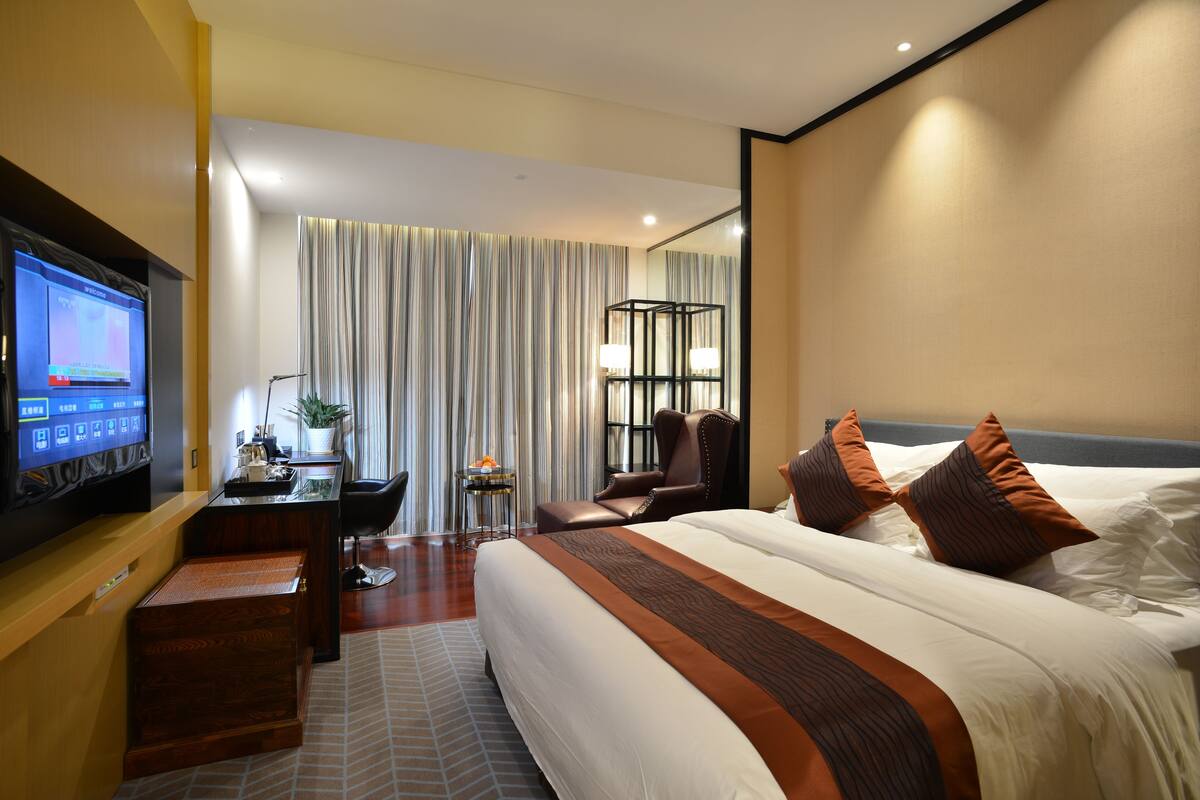Habitación de hotel con una cama grande, un escritorio, un televisor de pantalla plana, una silla y una mesita con una planta.