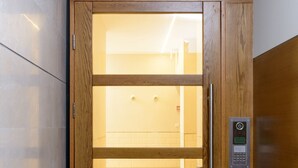 Uma porta de elevador de madeira com painel de controle digital, painel de vidro e design ripado acima.