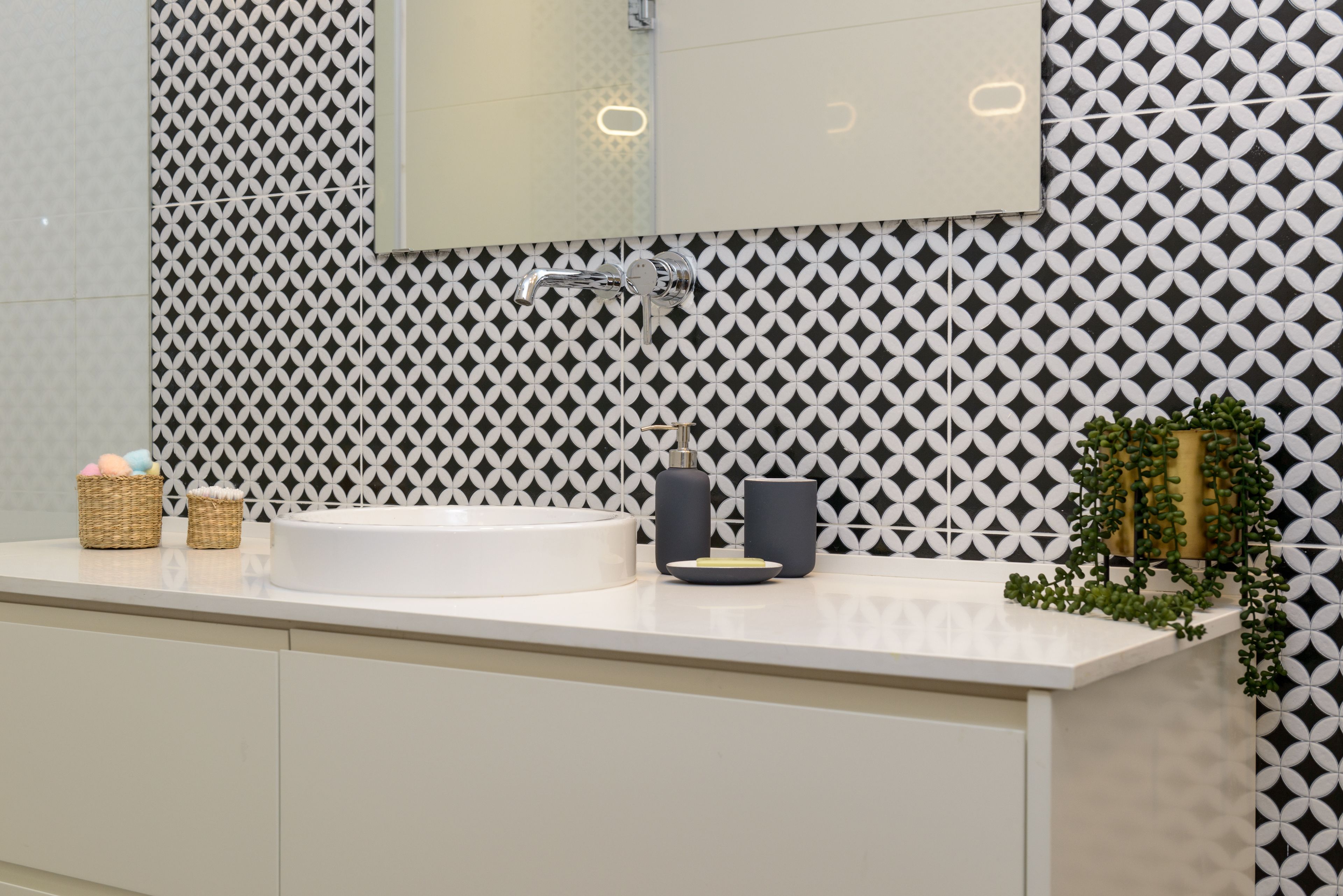 Une salle de bain moderne avec un lavabo blanc, un miroir et un mur à motifs.