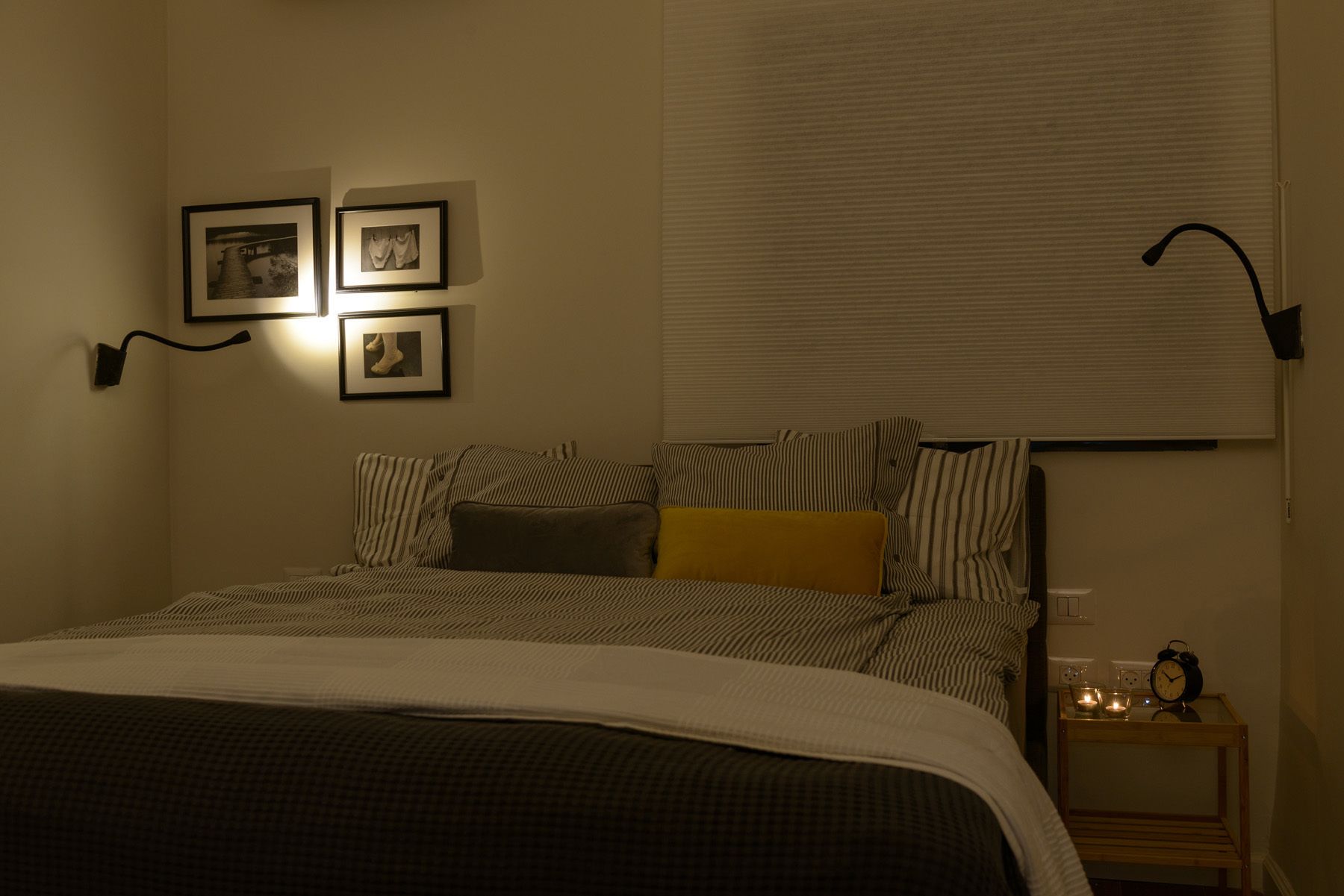 A bedroom with a bed, striped pillows, a bedside table with a clock, and wall-mounted pictures.