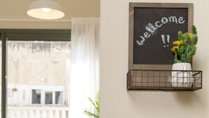 Um quarto com uma mesa e cadeiras de madeira, um quadro negro com a mensagem 'Welcome!' e um recipiente de metal cheio de limões.