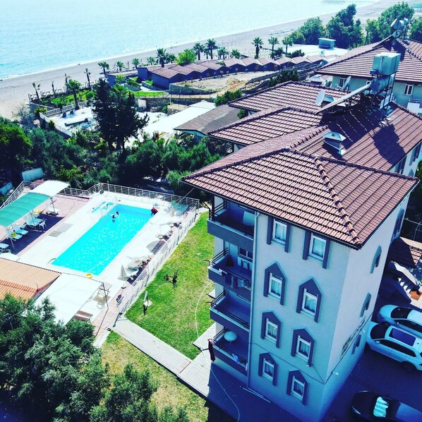 Un hotel de varios pisos con piscina en la azotea, vista a la playa y un estacionamiento.