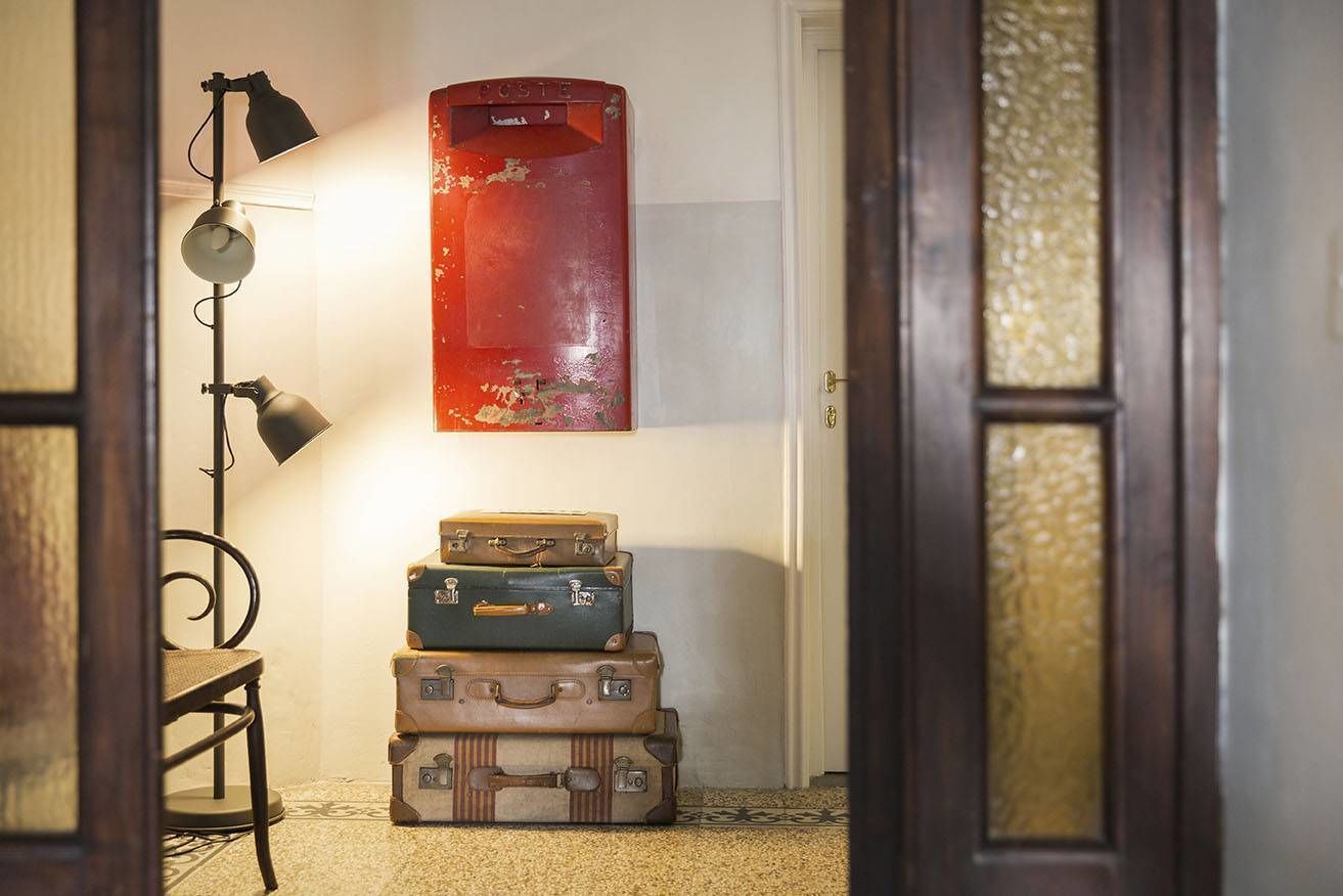 Un pasillo con una pila de maletas antiguas, un buzón rojo retro y una lámpara de pie.