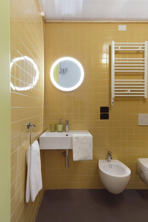 Un baño con baldosas amarillas, un lavabo blanco, un bidé y un perchero para toallas.