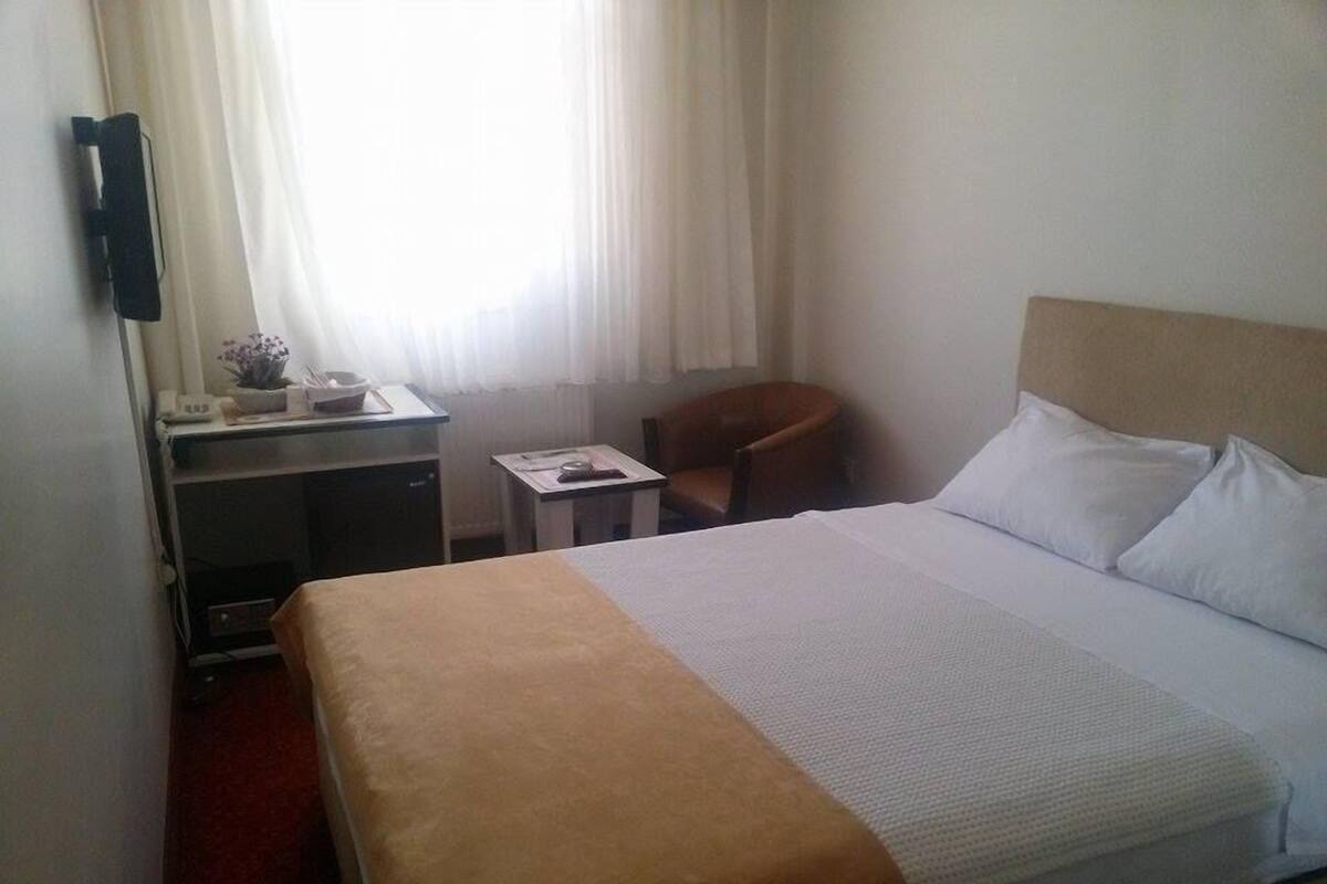 Une chambre d’hôtel avec un lit, un bureau, une chaise et une fenêtre avec des rideaux.
