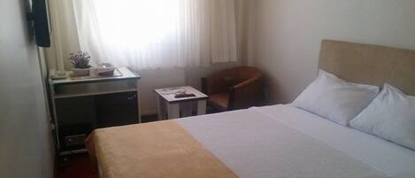 A hotel room with a bed, a desk, a chair, and a window with curtains.