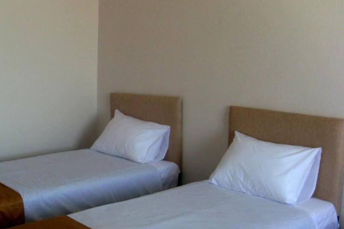 Deux lits simples avec du linge de lit blanc et des têtes de lit marron, dans une pièce aux murs de couleur neutre.