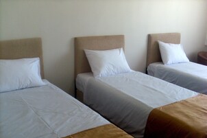 Tres camas individuales con cabeceras, ropa blanca y una pared lisa.