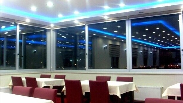 A restaurant with tables and chairs, large windows, and a ceiling with blue lighting. - Butik Ertur Hotel (Dogubayazit)