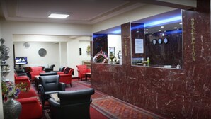 A reception area with a marble reception desk, red and black seating, and a television in the background. - Butik Ertur Hotel (Dogubayazit)