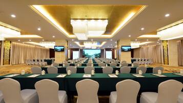 A conference room with rows of tables and chairs, a large screen at the front, and a chandelier.