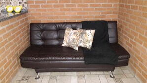 A brown leather sofa with a patterned pillow and a black throw blanket against a brick wall. - Toca Hospedaria (São Bento do Sapucaí)