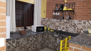 A kitchen with a microwave, a sink, and a yellow chair. - Toca Hospedaria (São Bento do Sapucaí)